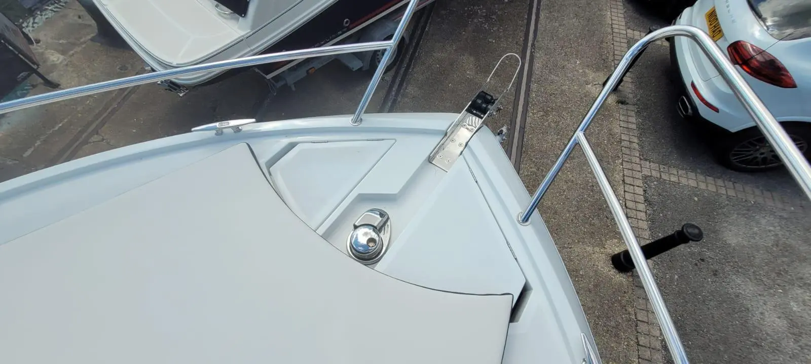 View from the bow of a boat showing a polished anchor system, railings, and nearby vehicles in a marina.
